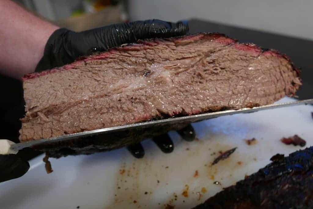 6 Tips For Taking Smoked Brisket From Average To Amazing 3 Man Holding A Sliced Smoked Brisket Over A White Cutting Board
